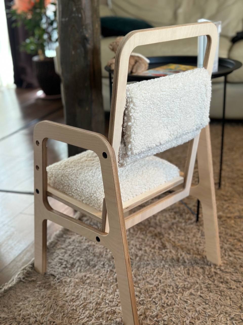 2. Back view of Luula adjustable children's chair in natural wood with vanilla lamb padding, on a textured rug