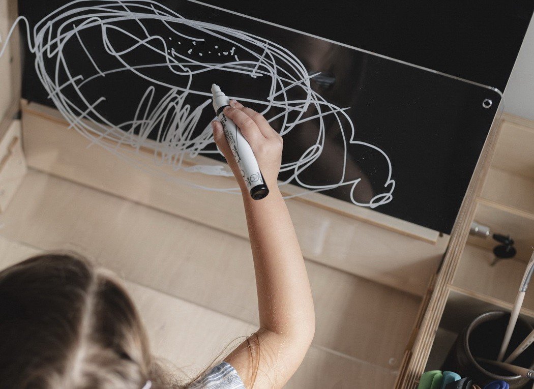 3. Child drawing on a transparent acrylic board attached to a Montessori table, highlighting creative play and learning.