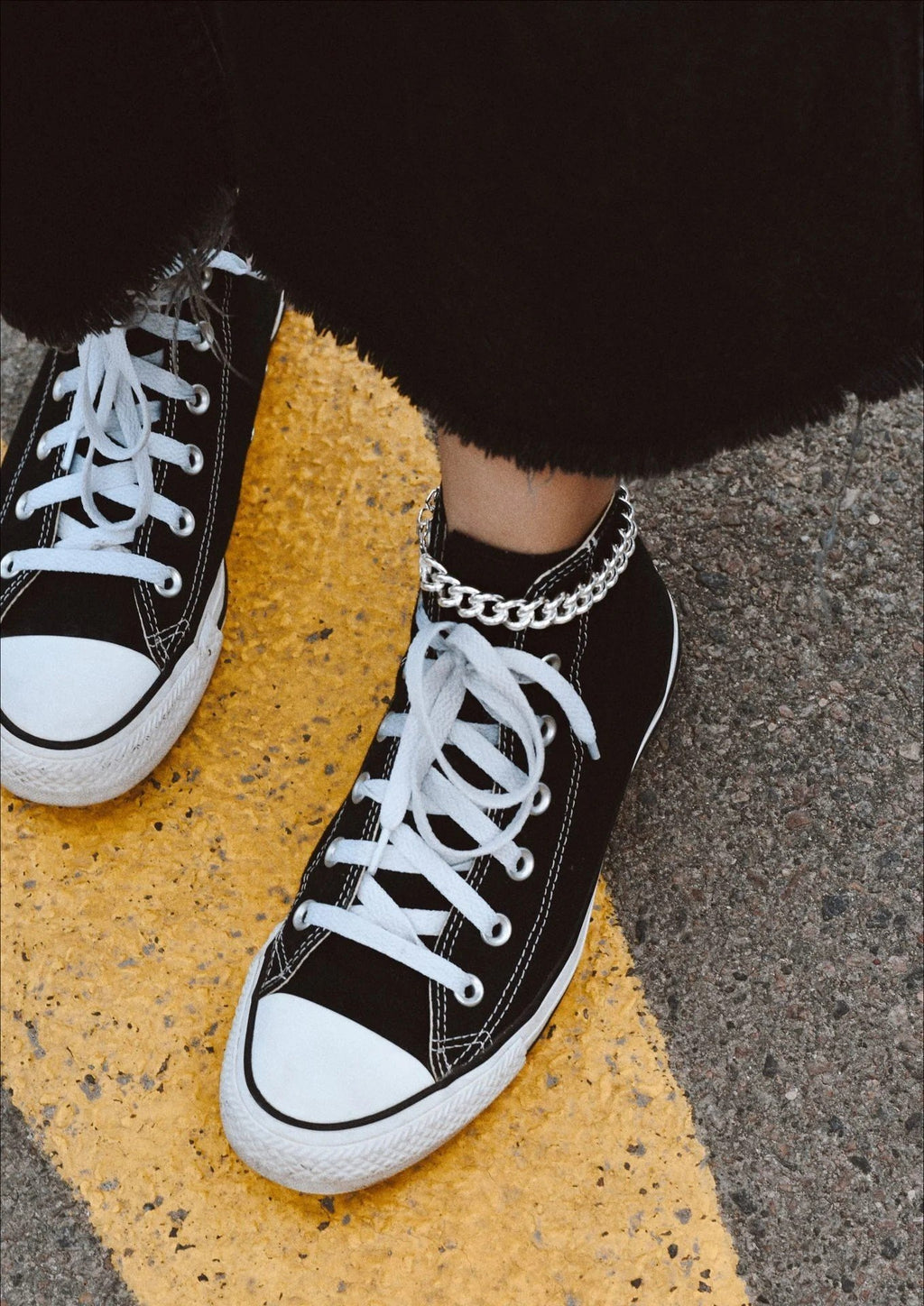 1. Person wearing black sneakers with a silver anchor anklet on a textured outdoor surface