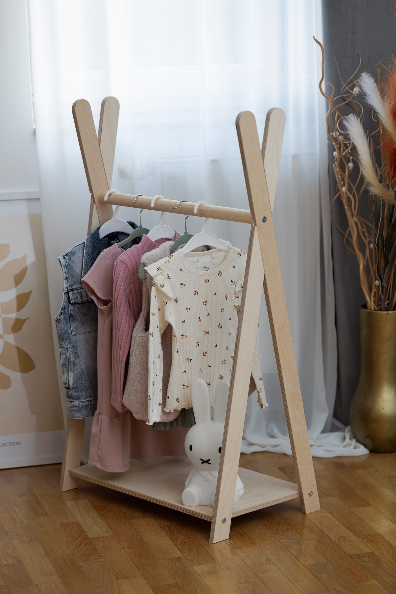 1. Natural wood children's clothing rack with assorted clothes and a white bunny toy in a stylish room