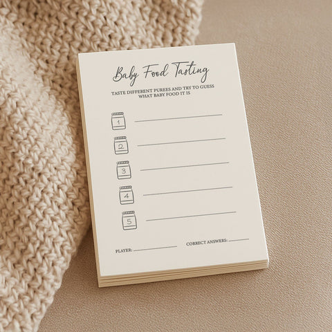 1. Stack of Beebila baby shower game cards for baby food tasting on a beige knitted blanket, featuring cream Munken Pure paper with spaces for guessing puree ingredients