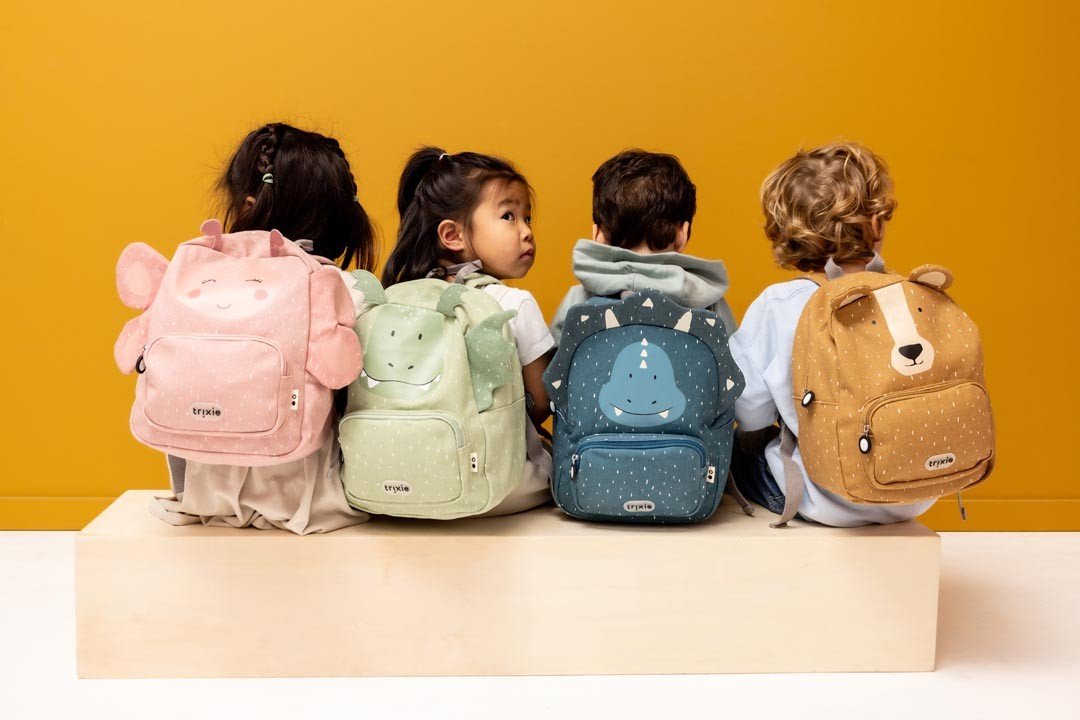 1. Four children with animal-themed backpacks including green dragon, sitting on bench, yellow background