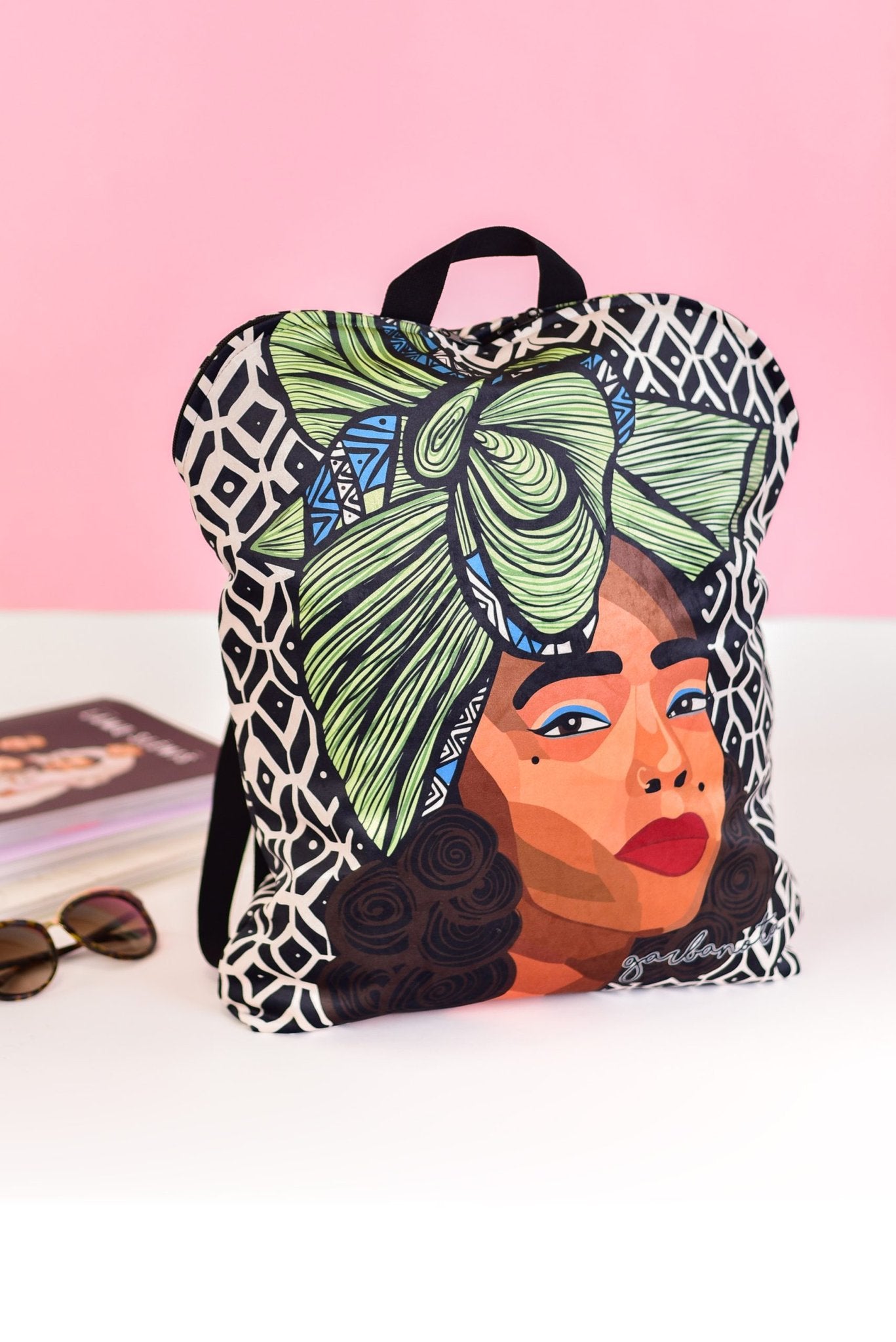 2. Garbanota BACKPACK TINA with unique Dovilė Aleksonė artwork, displayed on a table with a pink background
