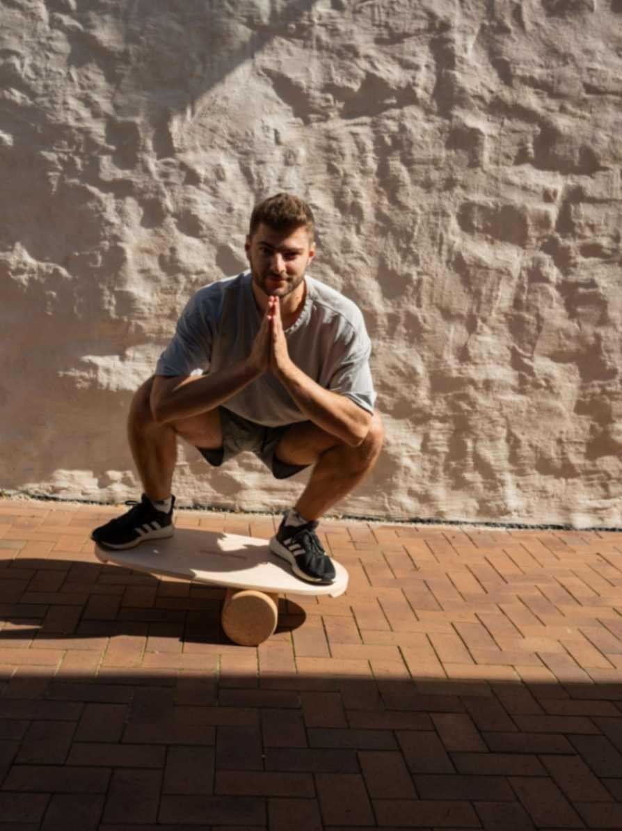 1. Man squatting on leg&go balance board with cork roller outdoors against a textured wall