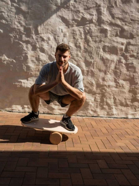 1. Man squatting on leg&go balance board with roller on brick pavement, wearing grey shirt and black sneakers