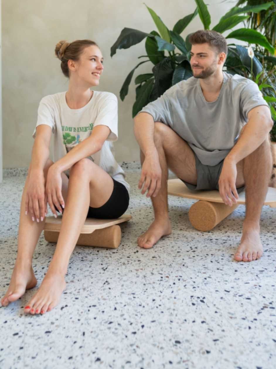 2. Man and woman sitting on round balance boards with exercise rolls indoors, smiling at each other