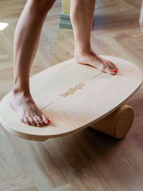 1. Woman balancing on leg&go round balance board with cork roller in a sunlit room, focusing on core strength