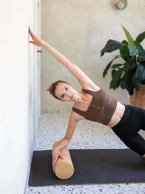 1. Woman using cork roller for side plank exercise against wall indoors
