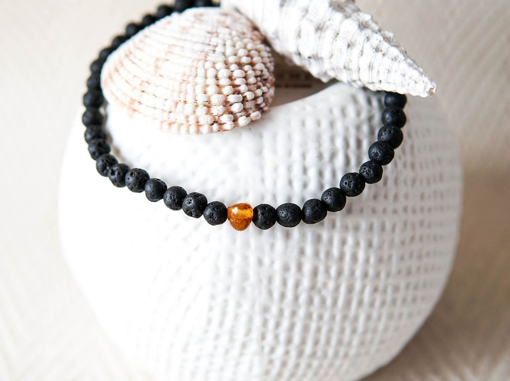 4. Close-up of men's Baltic Amber and Black Lava Bracelet by Canary Lava on textured surface with seashells