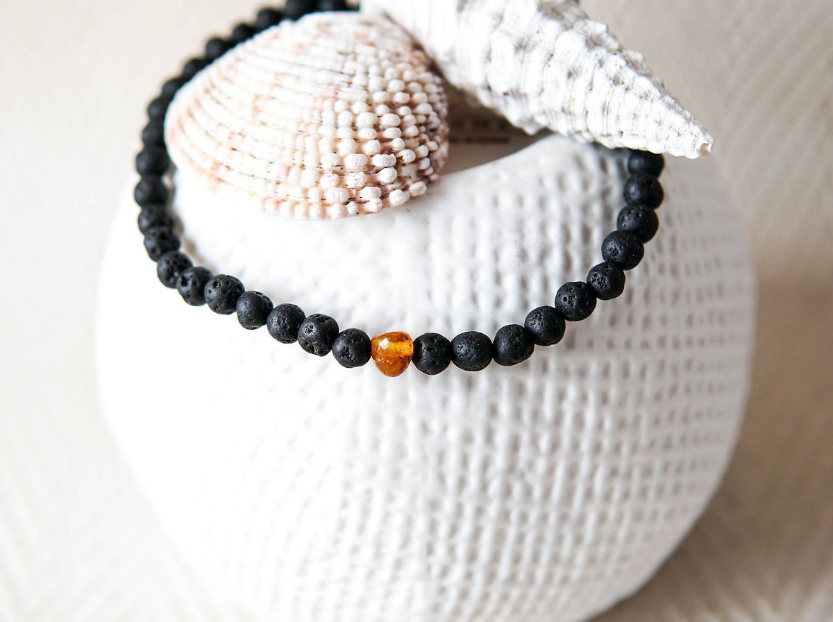 4. Close-up of men's Baltic Amber and Black Lava Bracelet by Canary Lava on textured surface with seashells