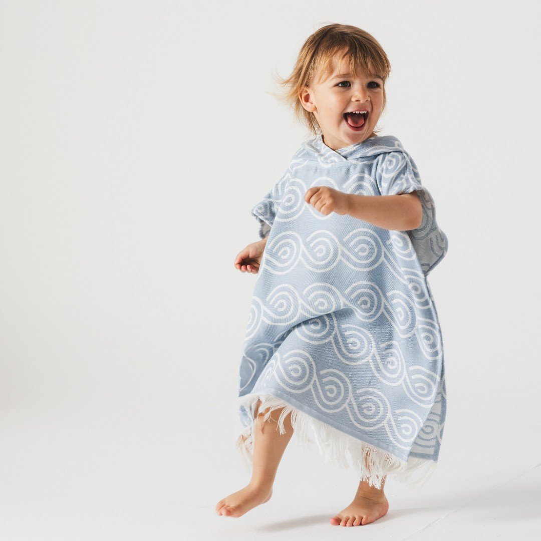 1. Child wearing light blue Patulove bamboo bath poncho with white swirl pattern, smiling and playing in a studio setting