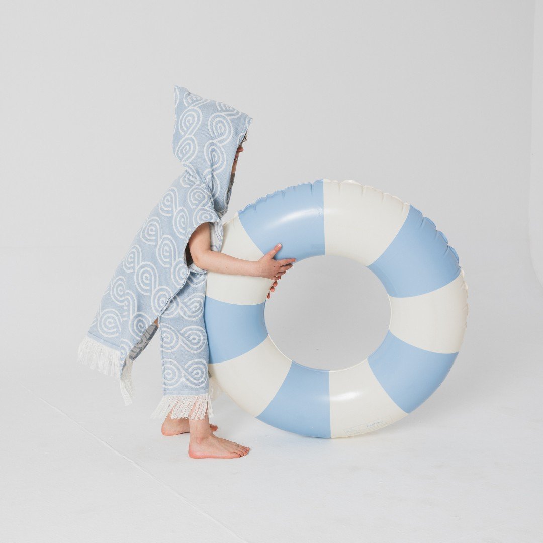 5. Child in light blue Patulove bamboo bath poncho with hood, holding large blue and white inflatable ring