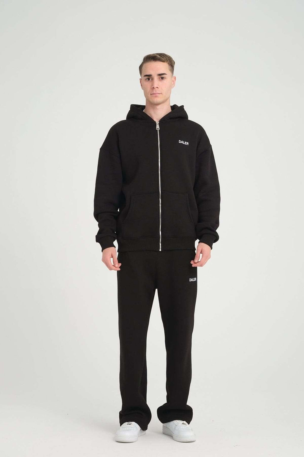 4. Man in black jogger pants and hoodie with DALER logo, facing forward in studio