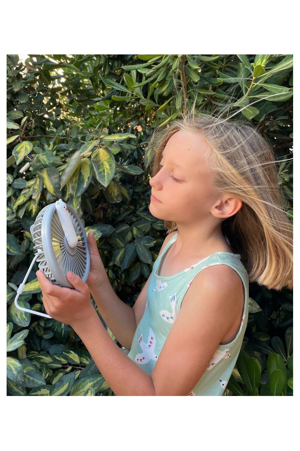 1. Child holding grey Little Bear Fan Lamp outdoors with greenery in background