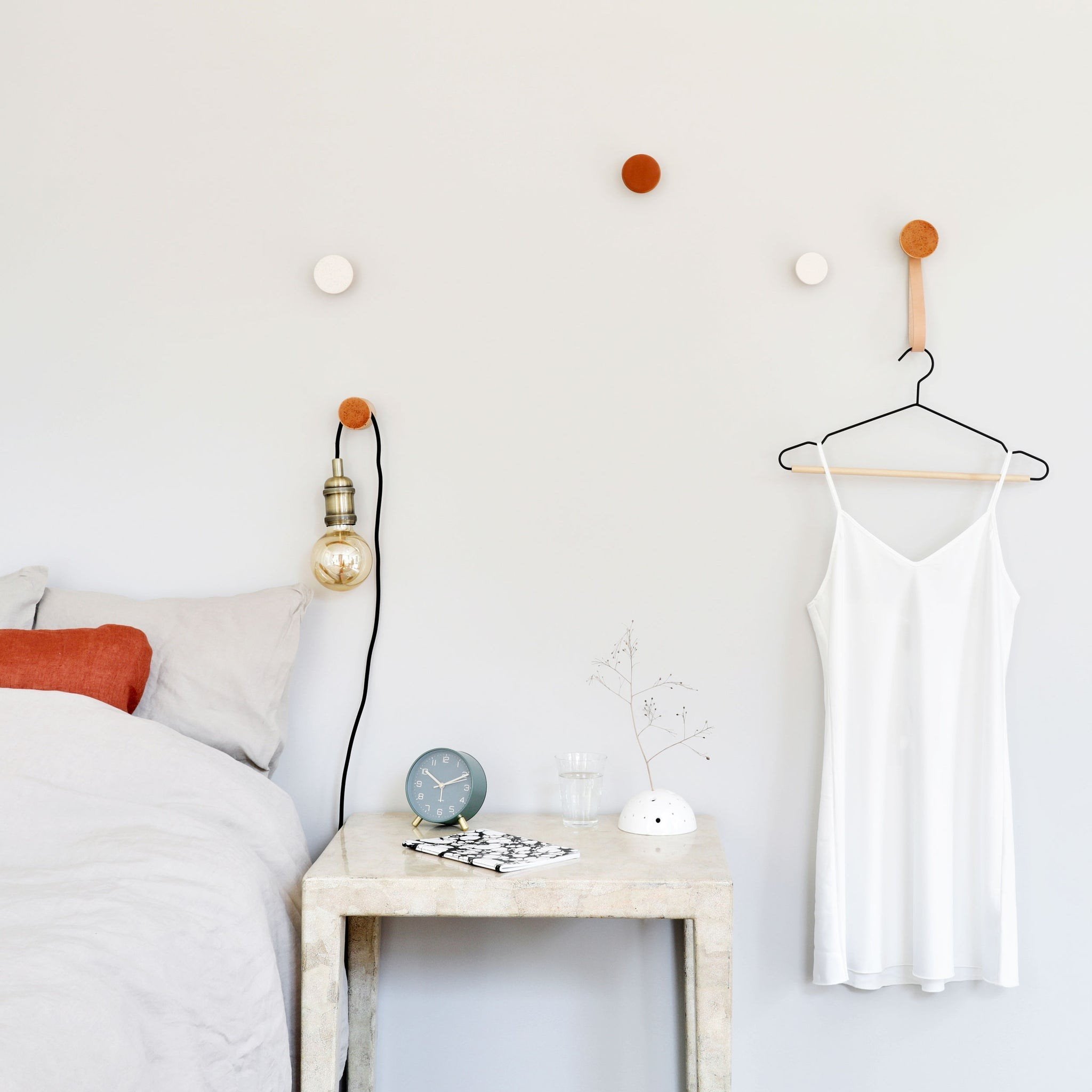 1. Lifestyle image of Beech Wood & Ceramic Wall Hooks by 5mm Paper in a bedroom setting, showcasing dark terracotta orange and white hooks used for hanging a dress and lamp