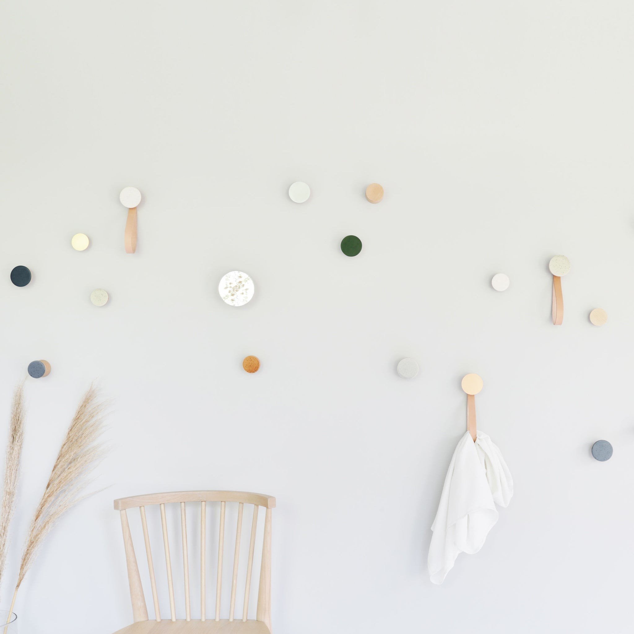 2. Lifestyle image of multiple Beech Wood & Ceramic Wall Hooks in various colors, including terracotta orange, used decoratively on a wall