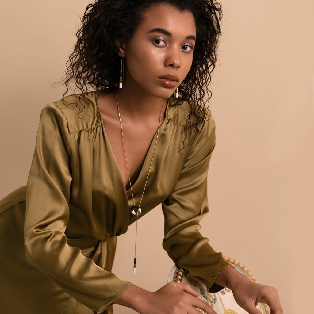1. Woman wearing SCULP Big OM Choker in black and white with 24K gold details, styled with a green dress in a lifestyle setting