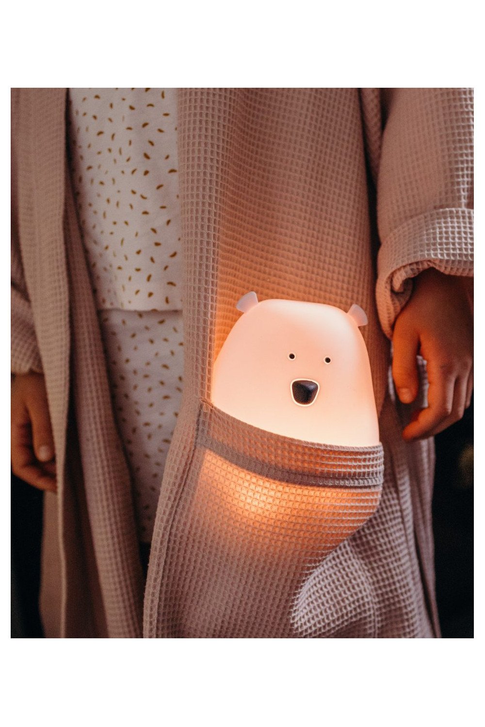 1. Child holding pink bear lamp in pocket of beige robe, providing warm glow