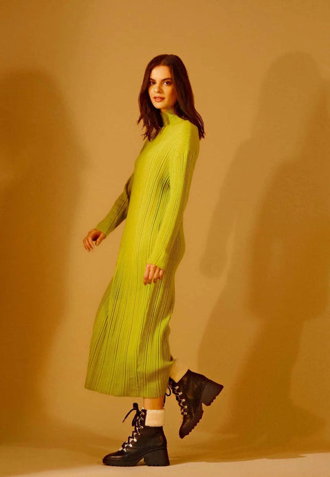 1. Woman in green dress wearing black combat boots with shearling detail, walking in studio setting