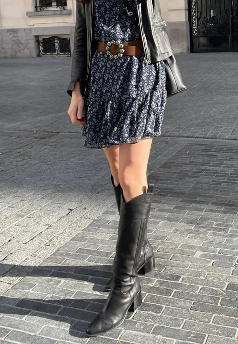 1. Woman wearing black knee-high leather boots with block heel paired with floral dress and leather jacket on urban street