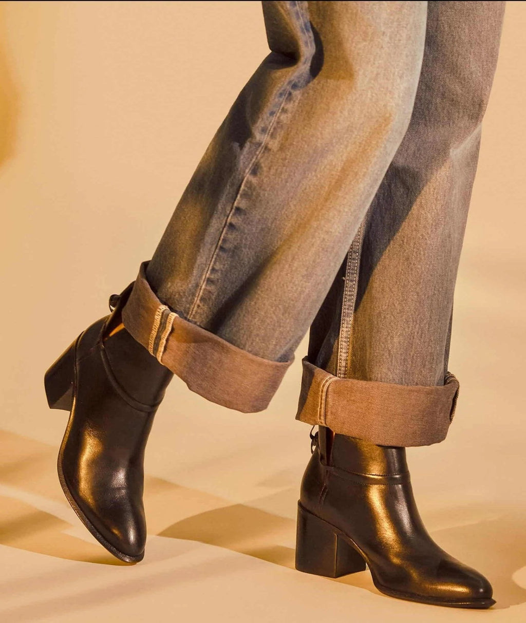 1. Woman wearing black leather ankle boots with block heel and rolled-up jeans in warm indoor setting