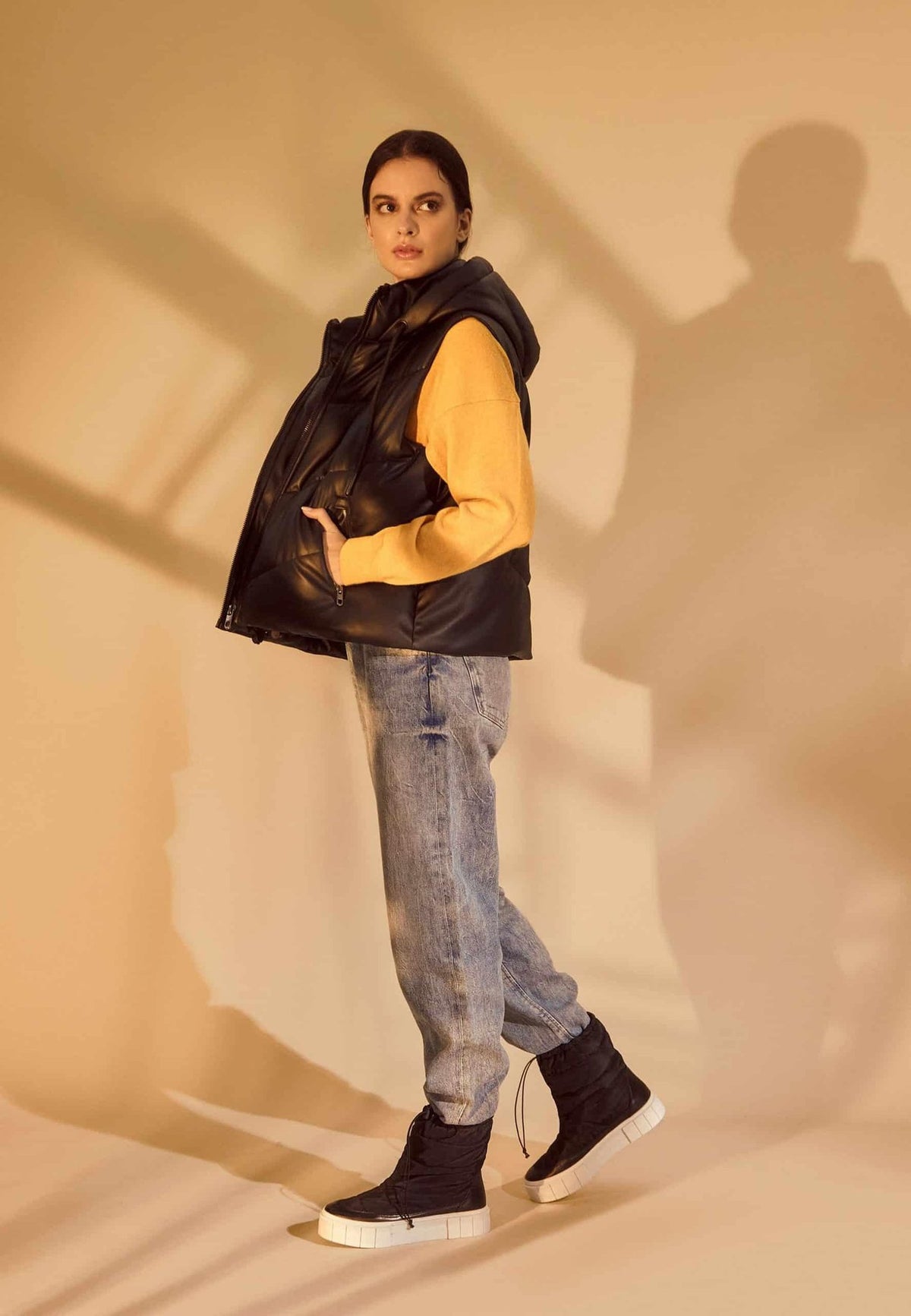 1. Woman in black nylon winter boots, jeans, and yellow sweater posing indoors