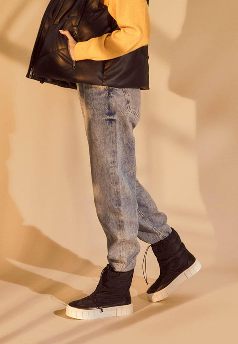 1. Woman wearing black nylon winter boots with jeans and yellow sweater in warm indoor setting