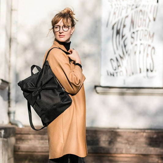 2. Woman with Muni Black Bow backpack in outdoor lifestyle setting, highlighting waterproof design