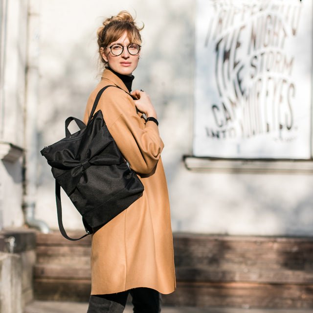 3. Woman carrying Muni Black Bow backpack, emphasizing stylish and practical design