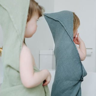 1. Two children wearing green and blue linen hooded towels standing in a bathroom