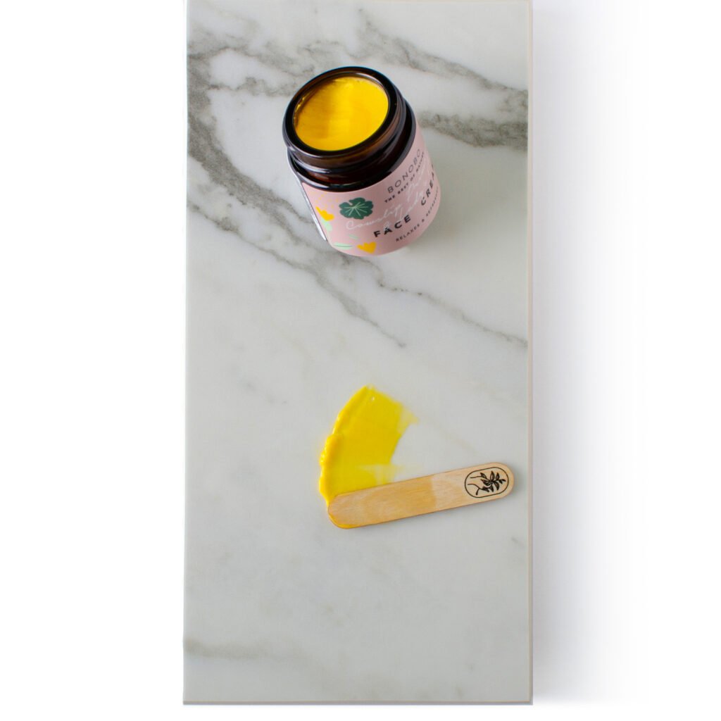 5. Open jar of BONOBO face cream with yellow cream and spatula on marble surface