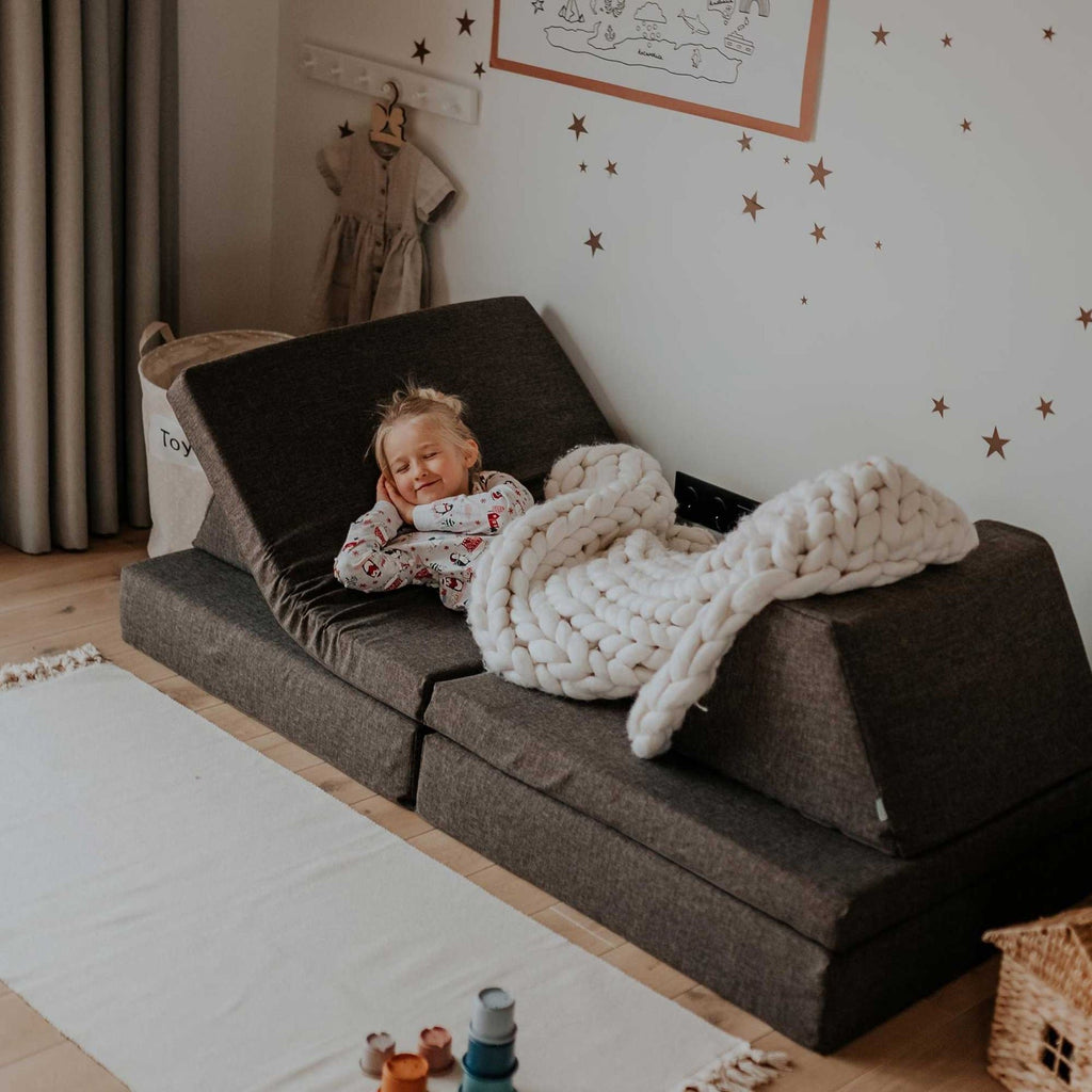 7. Child resting on Monboxy dark brown play mattress set with a blanket in a cozy room