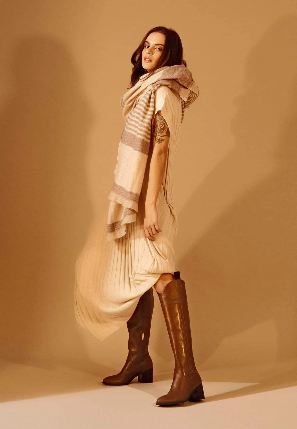 2. Woman in beige dress and scarf wearing brown knee-high leather boots with block heel, standing in a studio