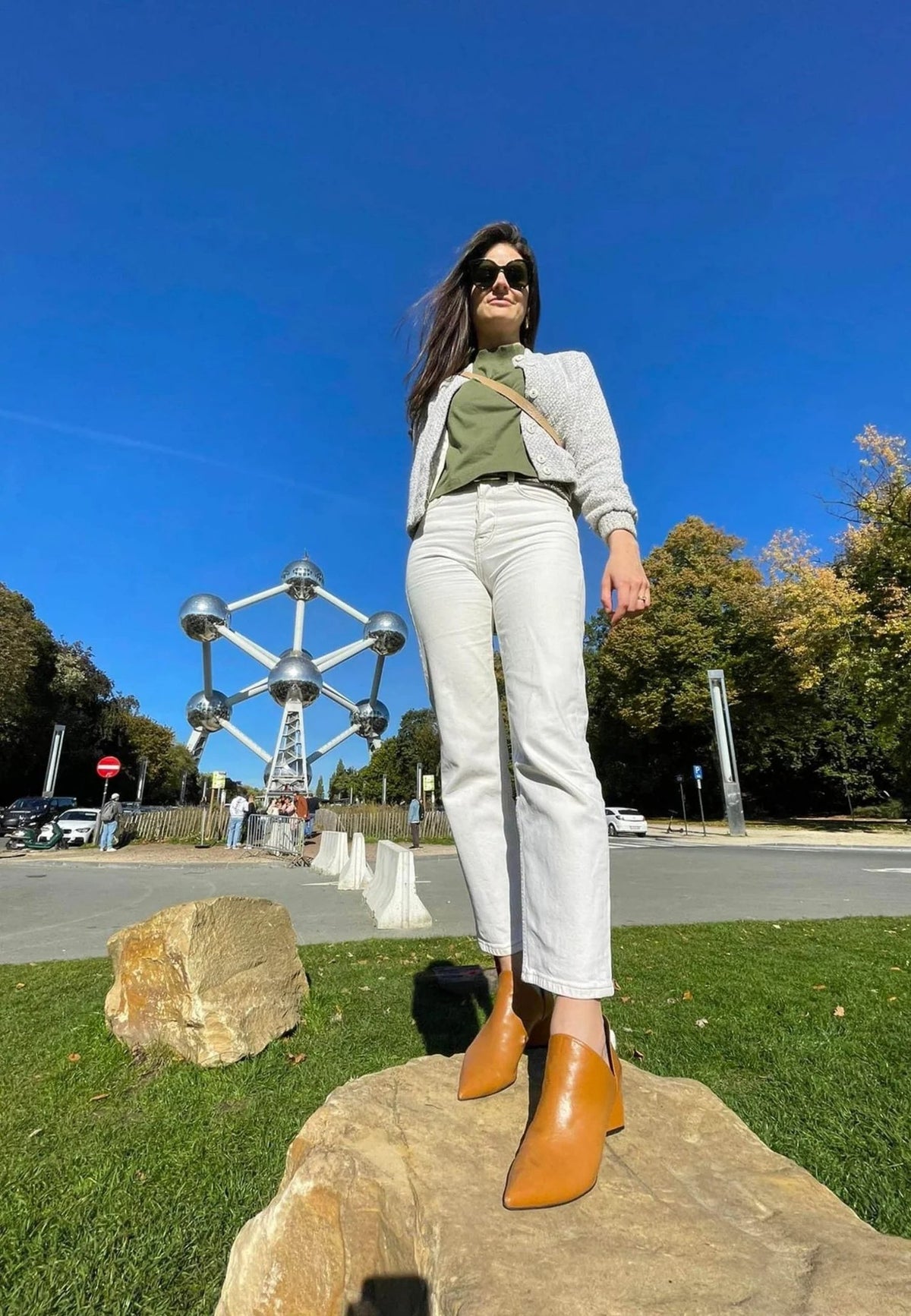1. Woman in white pants and brown leather ankle boots standing on rock with urban backdrop