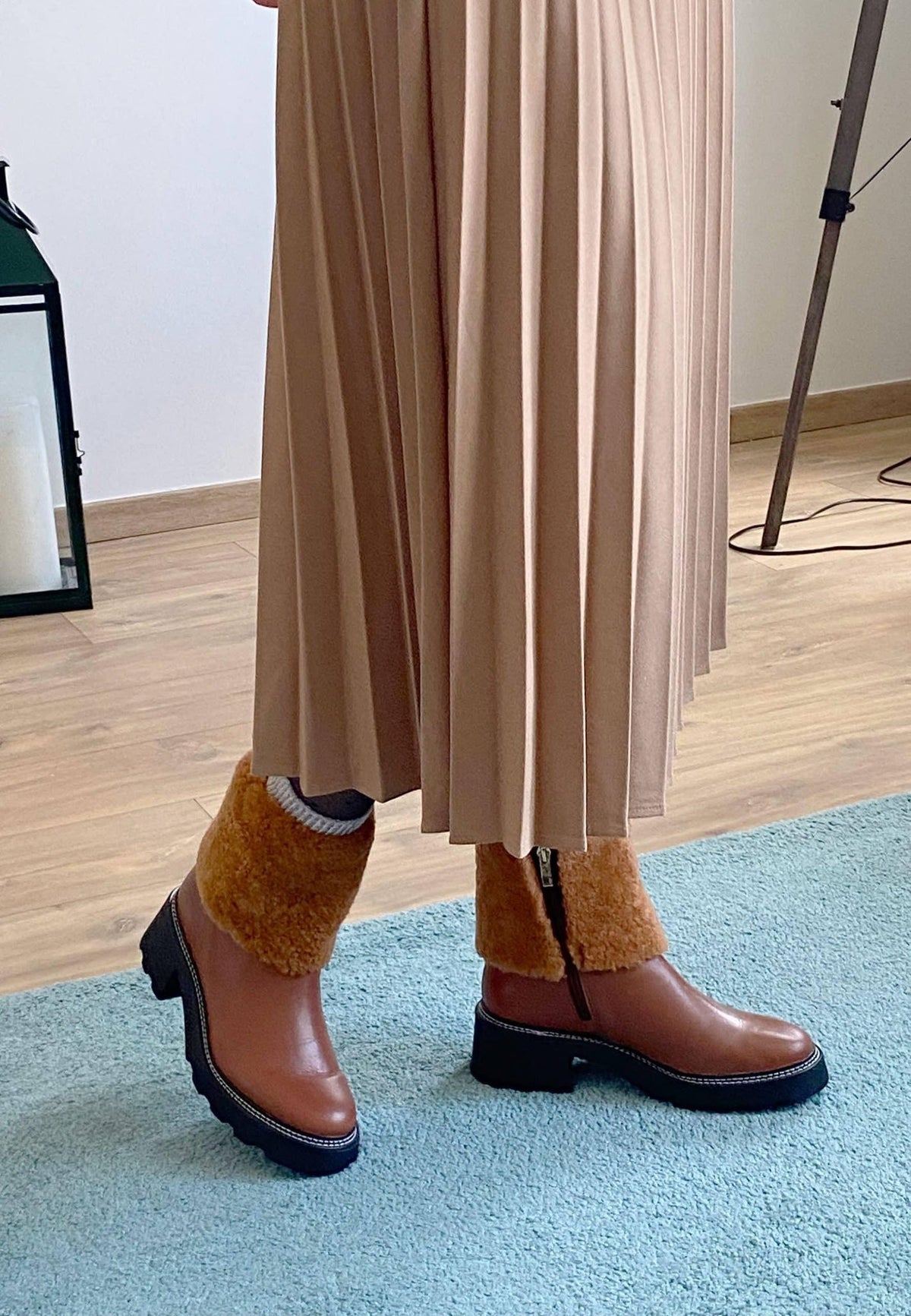 1. Woman wearing brown leather ankle boots with shearling detail and pleated skirt on wooden floor