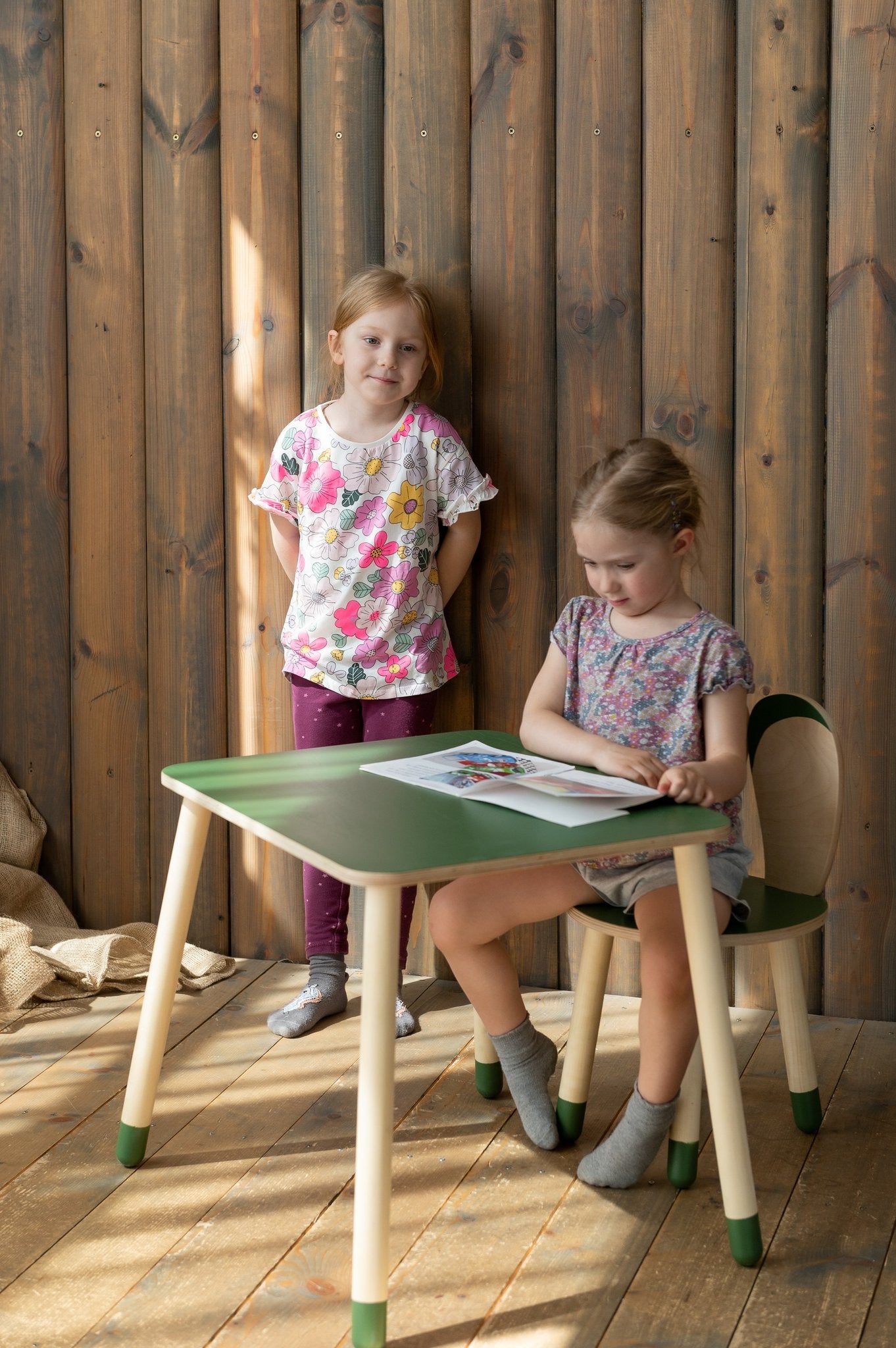 5. Two children using a green and natural wood bunny-themed table and chair set in a wooden room