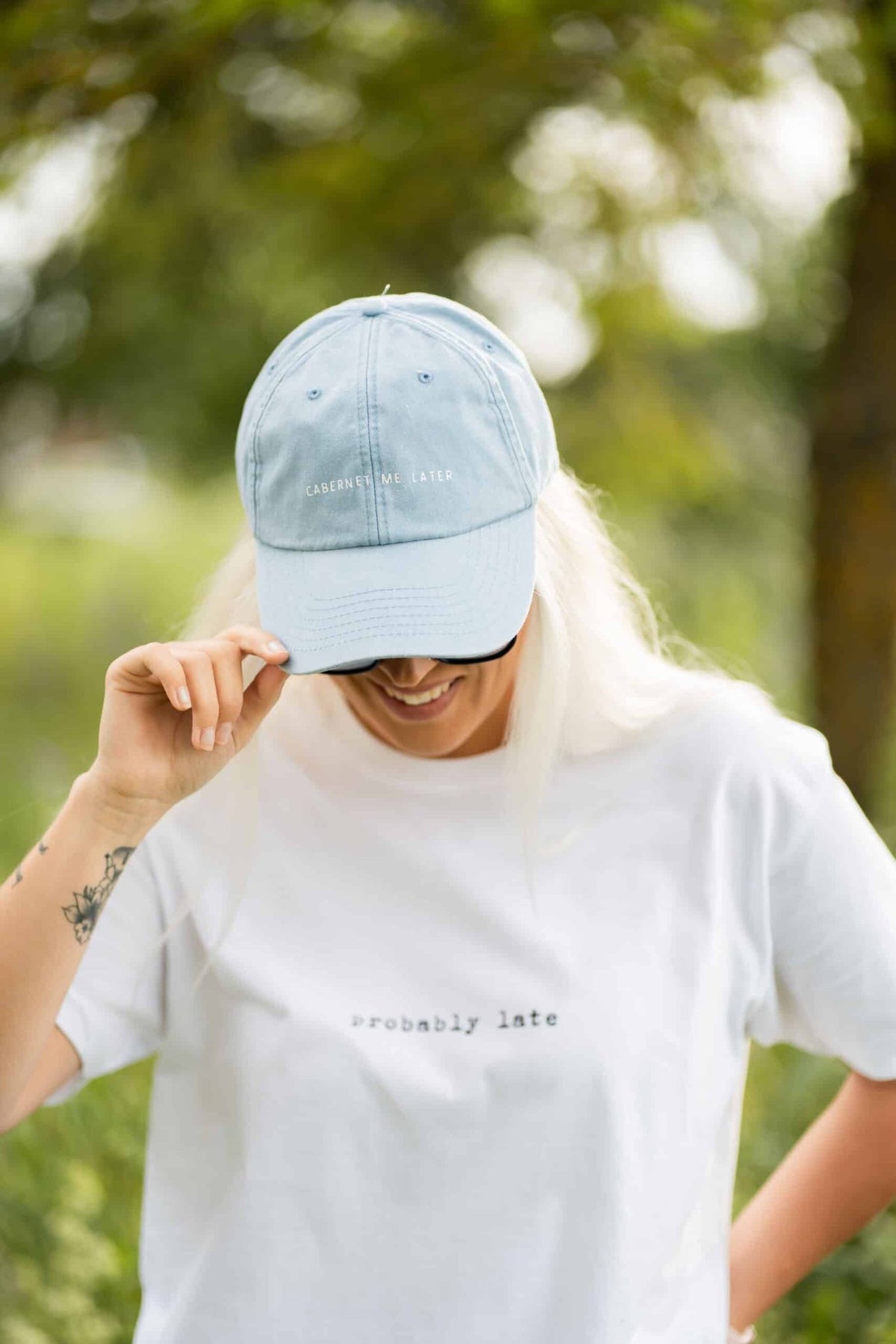 1. Woman wearing pastel blue cap with 'Cabernet Me Later' text, smiling in outdoor setting