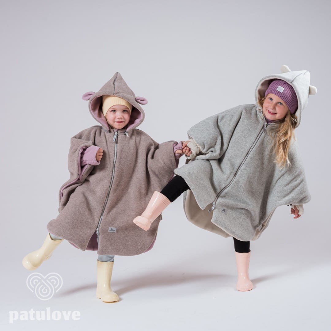 5. Two children wearing Patulove car ponchos, one pink lamb and one grey, holding hands in studio