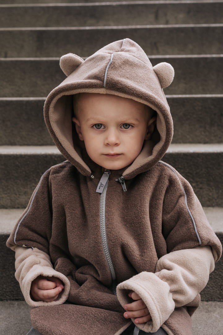 9. Child sitting on steps wearing brown Patulove car poncho with bear ears and hood