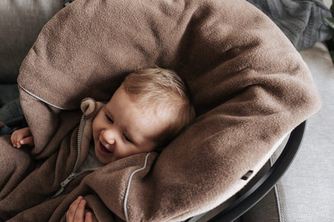 4. Baby smiling while wrapped in brown Patulove car poncho, lying on a soft surface