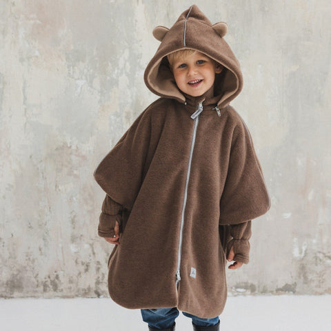 1. Child wearing brown Patulove car poncho with bear ears and hood, standing against a textured wall