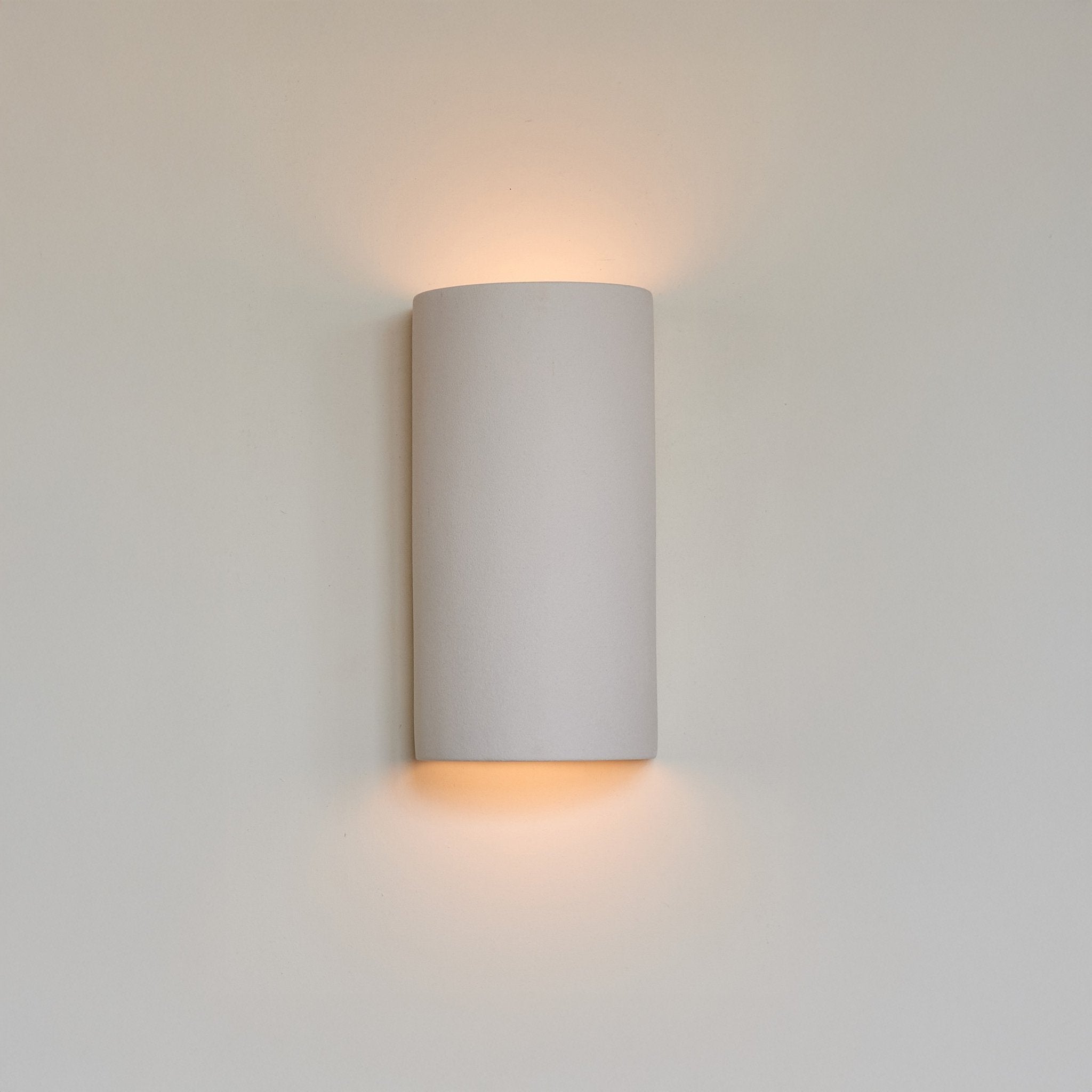 1. Extra matte white textured ceramic wall light by Ora, mounted on a wall, emitting a warm glow from top and bottom.