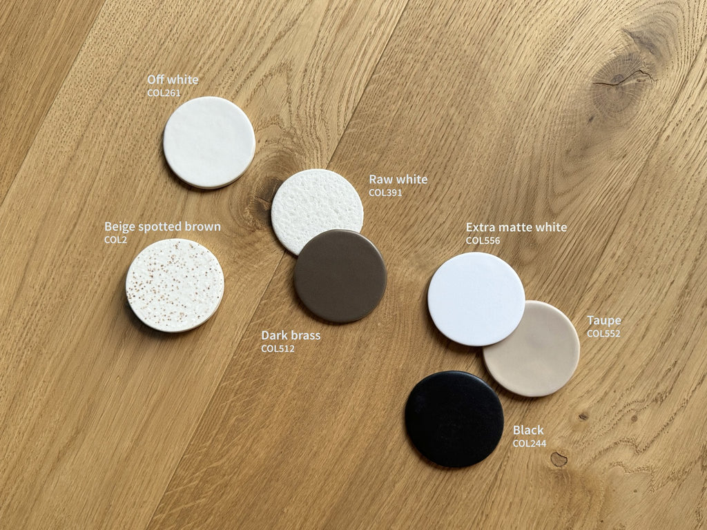 4. Flat lay of ceramic color samples including off-white, beige, and black on wooden surface