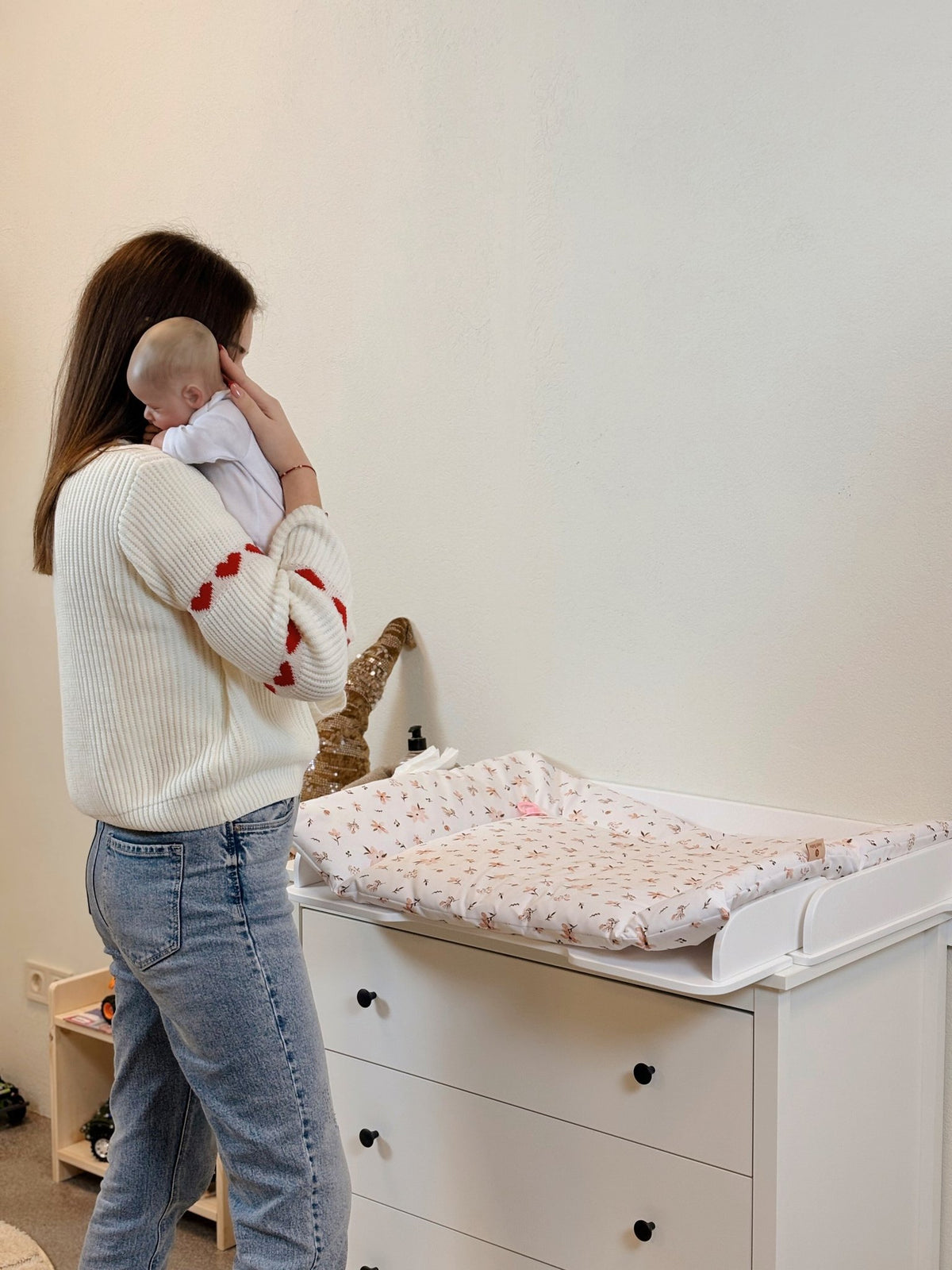 6. Woman holding baby near white changing table mat with colorful print