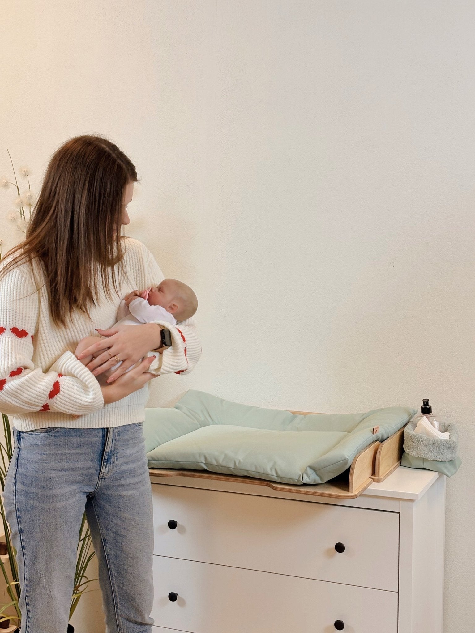 2. Woman holding baby next to green changing table mat on a dresser