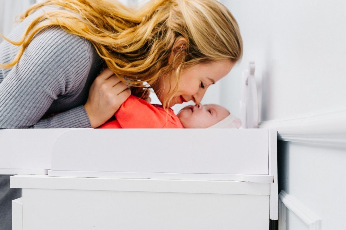 2. Woman smiling at baby on white changing table top in a nursery setting