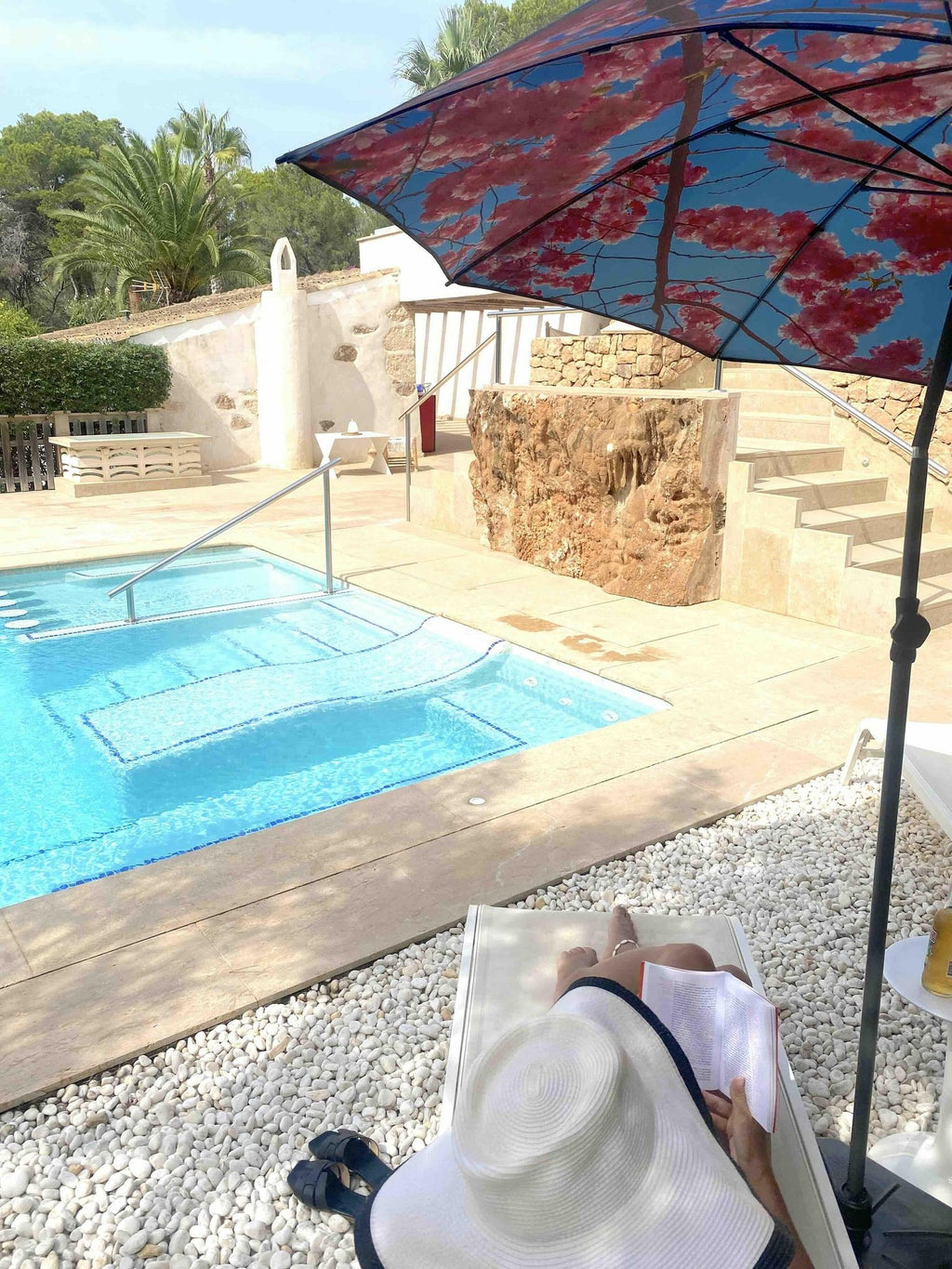 6. Cherry beach and terrace parasol with red floral print providing shade by a pool with a person relaxing on a sun lounger