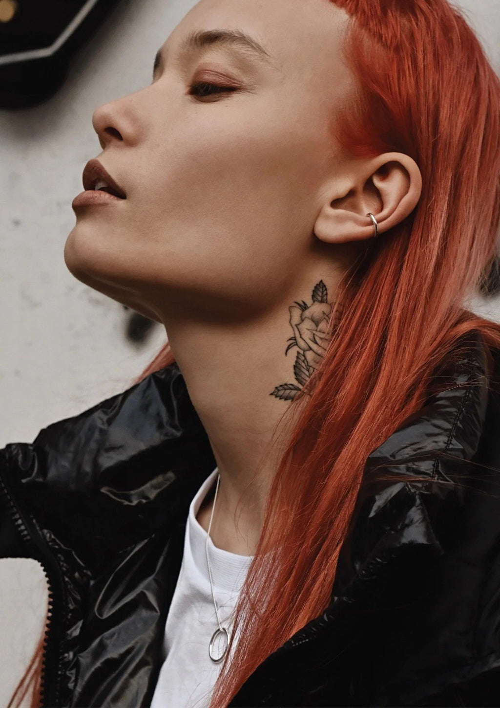 1. Woman with red hair wearing NO MORE silver circle necklace and black jacket, showing tattoo on neck