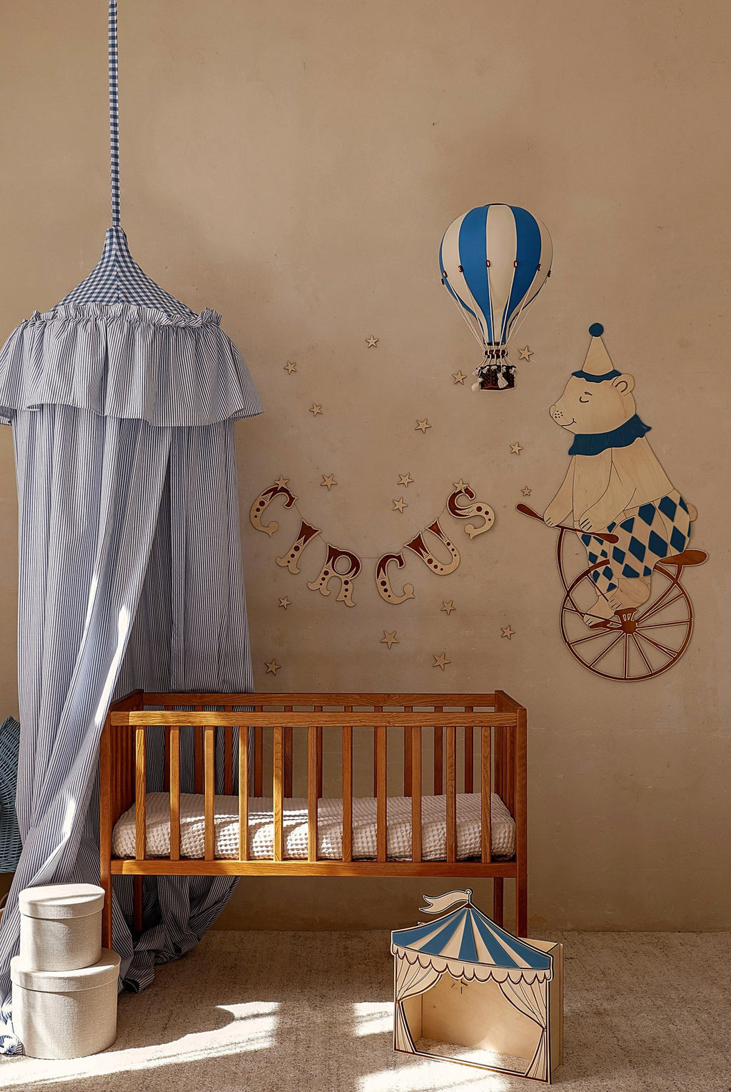 3. Nursery wall featuring a teddy bear on a bike, blue hot air balloon, and circus banner above a wooden crib with a blue canopy.