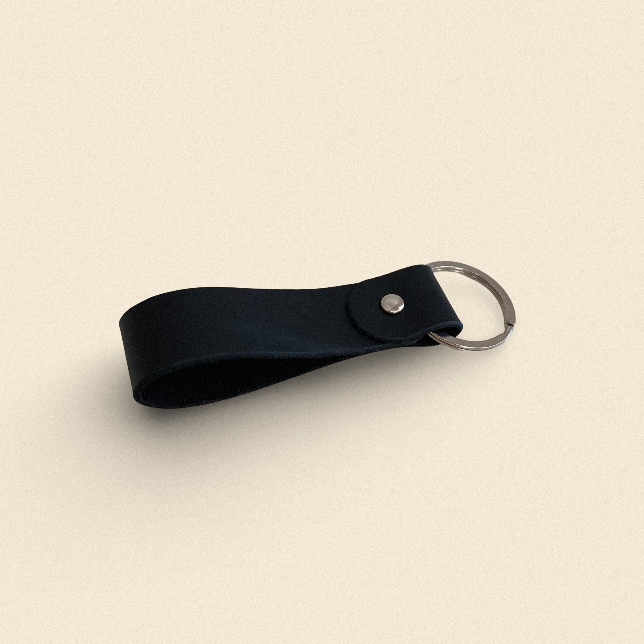 1. Black handmade leather keychain by Yoru with metal ring on beige background
